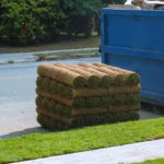 Installation of a modern landscape stacks of sod rolls for new lawn and dumpster full garbage container residential building construction home
