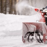 A man with a red snow-covered snow blower clears the area from snow. Clearing the area from snowfall.
