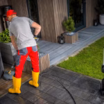 Caucasian Man in His 40s Pressure Washing Concrete Bricks Patio Using Washer Surface Attachment. Garden Maintenance.
